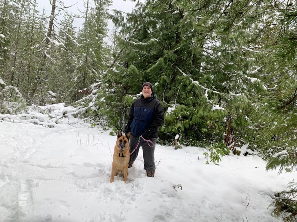German shepherd and man in cap in the snow in forest trees